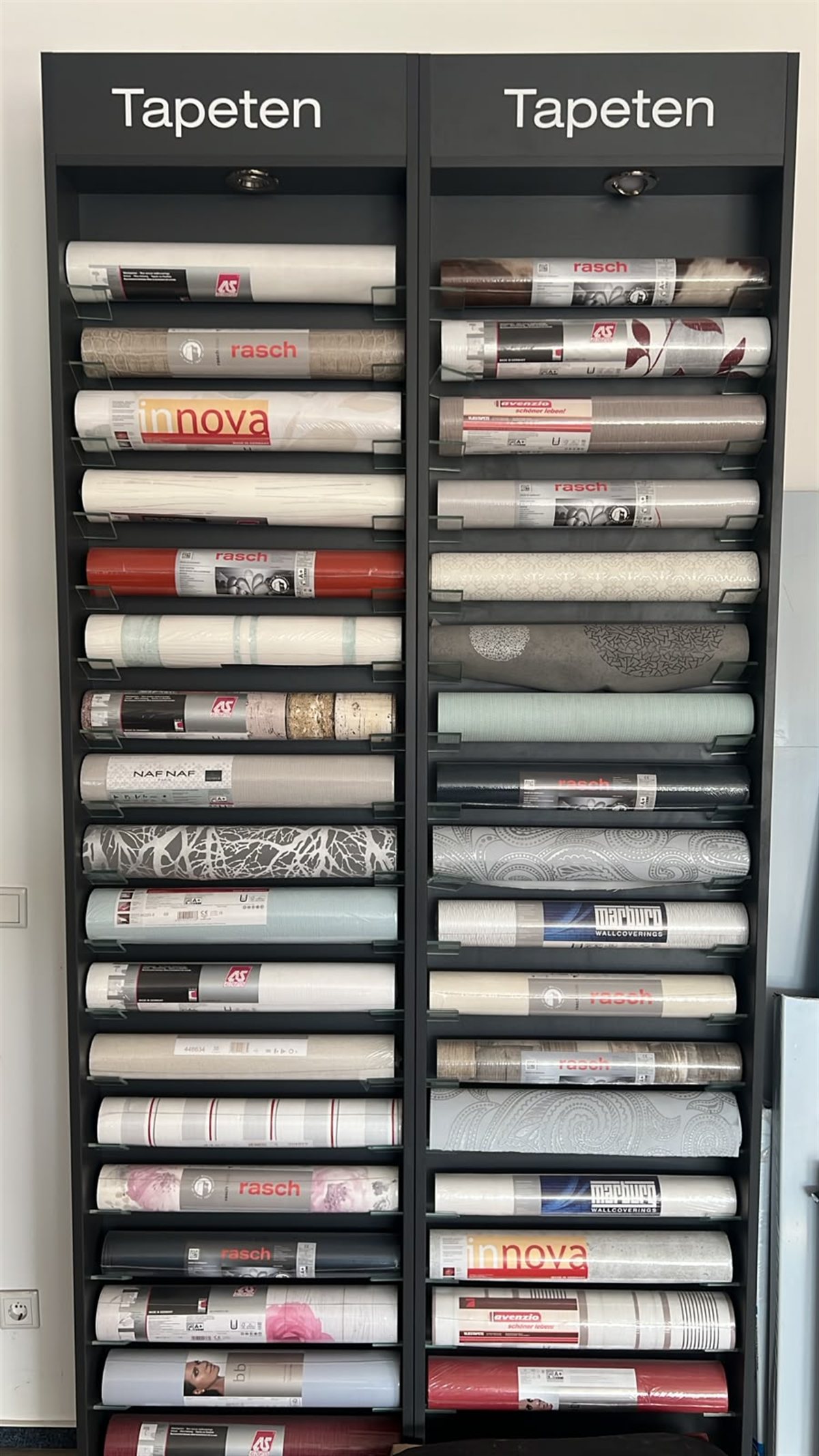 Tapetenregal mit sortierten Tapetenrollen in verschiedenen Mustern und Farben